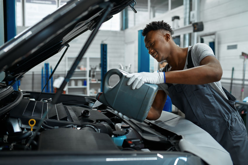 Male worker changes oil in engine, car service